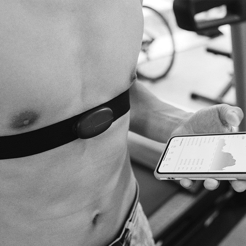 User wearing a Bluetooth waterproof heart rate monitor during a workout, tracking fitness progress on a smartphone.